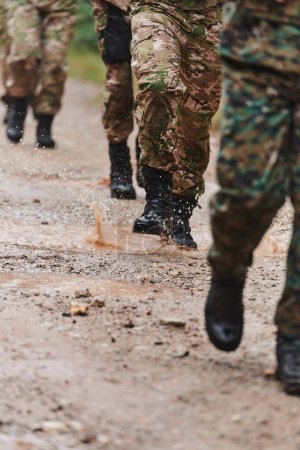 Close up photo, the resilient legs of elite soldiers, clad in camouflage boots, stride purposefully along a hazardous forest path as they embark on a high-stakes military mission. 