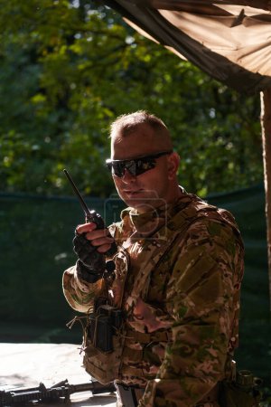 A military major employs a Motorola radio for seamless communication with his fellow soldiers during a tactical operation, showcasing professionalism and strategic coordination. 