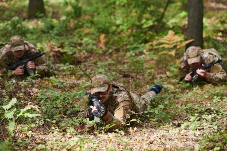 Foto de Soldados de élite maniobran sigilosamente a través del denso bosque, camuflados con equipo especializado, mientras se embarcan en una misión militar encubierta y estratégica.. - Imagen libre de derechos