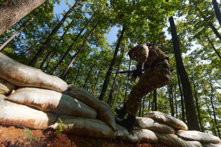 Photo for An elite soldier adeptly clears military barriers in the perilous wooded terrain, showcasing tactical skill and agility during specialized training. - Royalty Free Image
