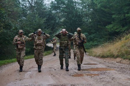 Un grupo de soldados de élite lleva cautivos a través de un campamento militar, mostrando un ambiente tenso de detención y operaciones de seguridad. 