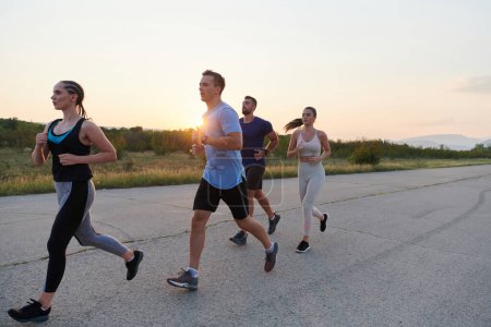 Foto de Un grupo diverso de corredores encuentra motivación e inspiración en el otro mientras entrenan juntos para una próxima competencia, en un escenario de puesta de sol impresionante. - Imagen libre de derechos