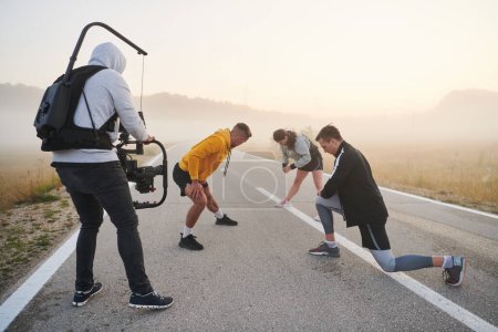 Ein erfahrener Videofilmer fängt die dynamische Szene ein, in der Sportler Aufwärm- und Dehnübungen zur Vorbereitung auf ihren morgendlichen Lauf absolvieren und dabei Hingabe und Teamwork hinter der Linse zeigen..