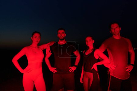 Foto de En las últimas horas de la noche, un diverso grupo de atletas exhaustos encuentran consuelo bajo un resplandor rojo, reflexionando sobre su viaje maratónico de un día y celebrando la camaradería en medio de la fatiga.. - Imagen libre de derechos