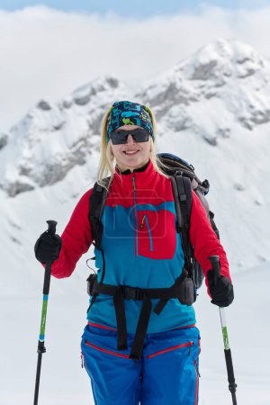 Ein entschlossener Skifahrer besteigt einen schneebedeckten Gipfel in den Alpen und trägt Backcountry-Ausrüstung für eine epische Abfahrt