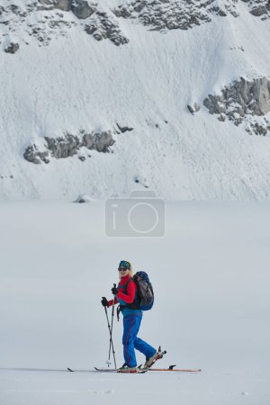 Ein entschlossener Skifahrer besteigt einen schneebedeckten Gipfel in den Alpen und trägt Backcountry-Ausrüstung für eine epische Abfahrt