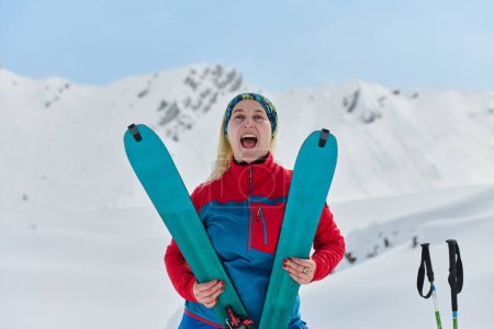 Téléchargez les photos : Une skieuse triomphante rayonne avec confiance au sommet d'un sommet enneigé après avoir conquis une ascension difficile. - en image libre de droit