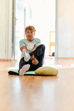 Téléchargez les photos : Dans un espace ensoleillé, une femme âgée pratique gracieusement le yoga rajeunissant, se concentrant sur les étirements du cou, du dos et des jambes, incarnant la sérénité et le bien-être.. - en image libre de droit