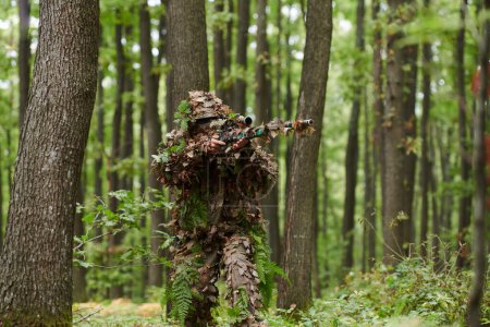 A highly skilled elite sniper, camouflaged in the dense forest, stealthily maneuvers through dangerous woodland terrain on a covert and precise mission. 
