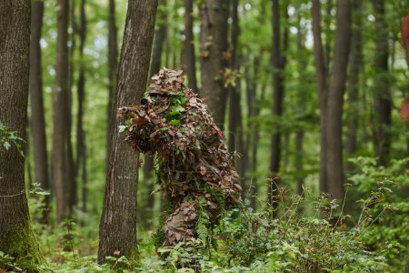 Téléchargez les photos : Un tireur d'élite hautement qualifié, camouflé dans la forêt dense, manœuvre furtivement à travers un terrain boisé dangereux sur une mission secrète et précise. - en image libre de droit