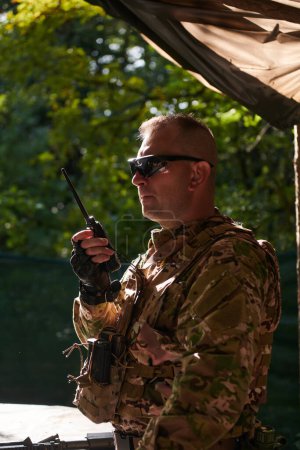 Photo for A military major employs a Motorola radio for seamless communication with his fellow soldiers during a tactical operation, showcasing professionalism and strategic coordination. - Royalty Free Image