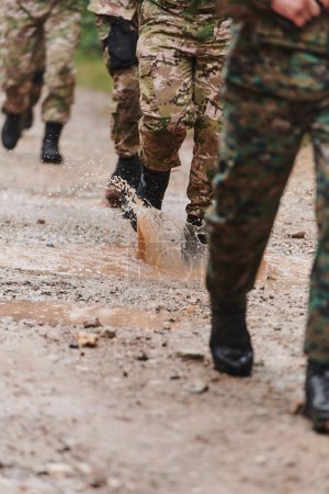 Foto de De cerca la foto, las piernas resistentes de los soldados de élite, vestidos con botas de camuflaje, caminan a propósito a lo largo de un peligroso sendero forestal mientras se embarcan en una misión militar de alto riesgo. - Imagen libre de derechos