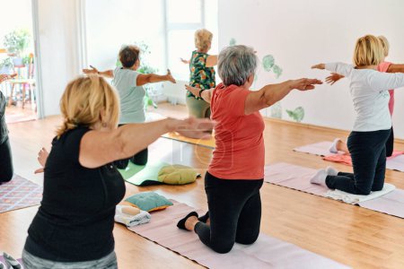Photo for A group of senior women engage in various yoga exercises, including neck, back, and leg stretches, under the guidance of a trainer in a sunlit space, promoting well-being and harmony. - Royalty Free Image