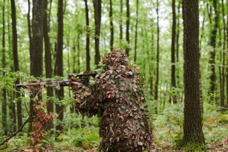 Foto de Un francotirador de élite altamente calificado, camuflado en el denso bosque, maniobra sigilosamente a través de terrenos forestales peligrosos en una misión encubierta y precisa. - Imagen libre de derechos