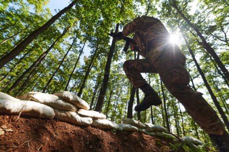 An elite soldier adeptly clears military barriers in the perilous wooded terrain, showcasing tactical skill and agility during specialized training. 