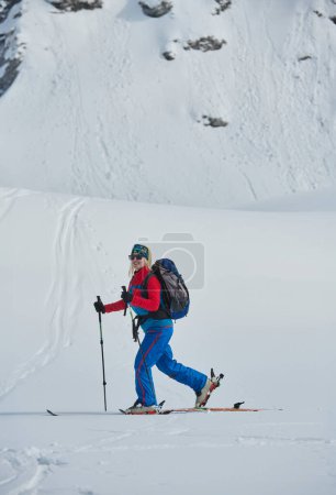 Foto de Una esquiadora se encuentra en la cima nevada de una montaña, equipada con equipo profesional y esquís, preparada para un emocionante descenso - Imagen libre de derechos