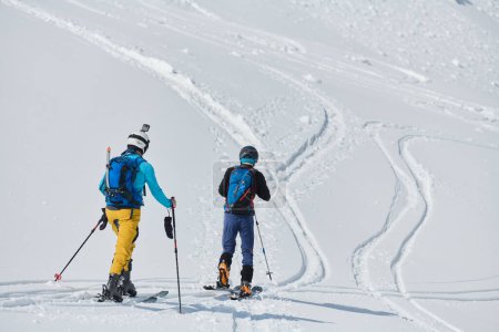 Foto de En una muestra de inquebrantable trabajo en equipo y determinación, dos esquiadores profesionales ascienden a los picos nevados de los Alpes, unidos en su búsqueda de la cumbre. - Imagen libre de derechos