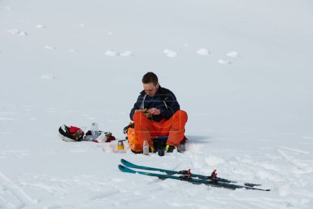 Ein Skifahrer hält auf einem schneebedeckten Grat inne, um einen Moment der Ruhe zu genießen und das atemberaubende Alpenpanorama zu genießen. 