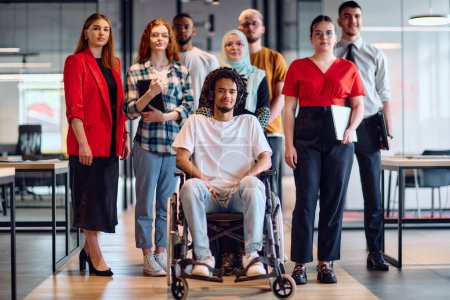 Photo for A diverse group of young business people walking a corridor in the glass-enclosed office of a modern startup, including a person in a wheelchair and a woman wearing a hijab. - Royalty Free Image