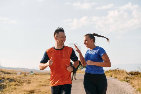 Photo for A couple dressed in sportswear runs along a scenic road during an early morning workout, enjoying the fresh air and maintaining a healthy lifestyle. - Royalty Free Image