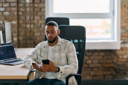  Empresario afroamericano se toma un descanso en una oficina moderna, utilizando un teléfono inteligente para navegar por las redes sociales, capturando un momento de conectividad digital y relajación en medio de sus esfuerzos empresariales