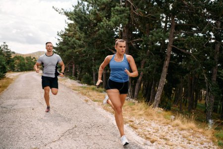 Photo for A couple dressed in sportswear runs along a scenic road during an early morning workout, enjoying the fresh air and maintaining a healthy lifestyle. - Royalty Free Image