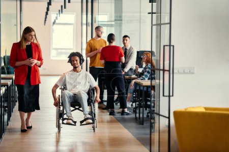 Photo for A diverse group of young professionals, including businesswomen and an African-American entrepreneur in a wheelchair, engage in collaborative discussion on various business projects in a modern - Royalty Free Image