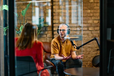 Photo for A gathering of young business professionals, some seated in a glass-walled office, engage in a lively conversation and record an online podcast, embodying modern collaboration and dynamic interaction - Royalty Free Image