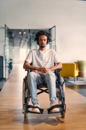 An African-American young entrepreneur in a wheelchair is surrounded by his business colleagues in a modern office setting, embodying diversity and collaboration in the workplace. 