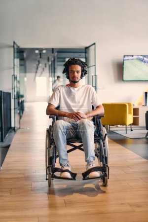 An African-American young entrepreneur in a wheelchair is surrounded by his business colleagues in a modern office setting, embodying diversity and collaboration in the workplace. 