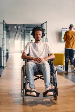 Un joven empresario afroamericano en silla de ruedas está rodeado por sus colegas de negocios en un entorno de oficina moderno, que encarna la diversidad y la colaboración en el lugar de trabajo. 