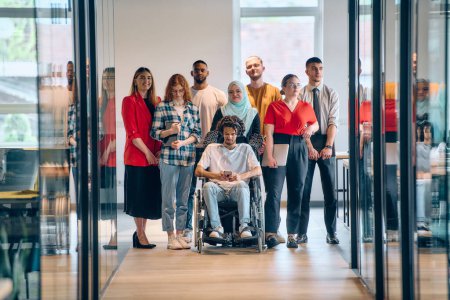 Téléchargez les photos : Un groupe diversifié de jeunes gens d'affaires se rassemble au sein d'un bureau vitré moderne de startups, mettant en vedette l'inclusion avec une personne en fauteuil roulant, un jeune homme afro-américain et un hijab - en image libre de droit
