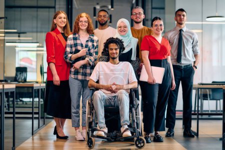 Un grupo diverso de jóvenes empresarios que caminan por un pasillo en la oficina acristalada de una startup moderna, incluida una persona en silla de ruedas y una mujer con un hijab.