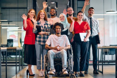 Un grupo diverso de jóvenes empresarios que caminan por un pasillo en la oficina acristalada de una startup moderna, incluida una persona en silla de ruedas y una mujer con un hijab.