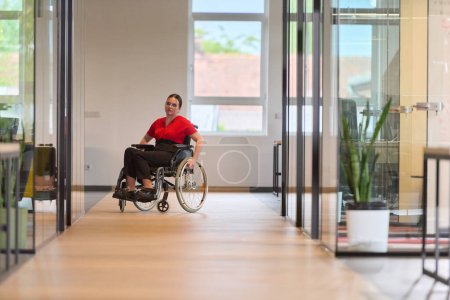 Téléchargez les photos : Une jeune femme d'affaires moderne en fauteuil roulant est entourée d'un espace de travail inclusif avec des bureaux vitrés, incarnant la détermination et l'innovation dans le monde des affaires. - en image libre de droit