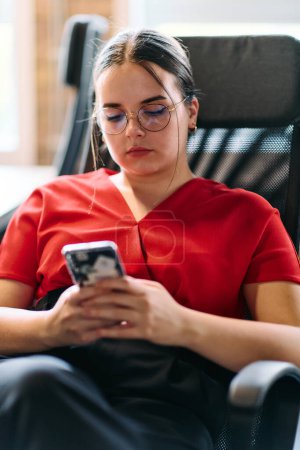 Photo for A businesswoman resting on a short break from work in a modern startup coworking center, using her smartphone to unwind and recharge. - Royalty Free Image