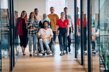 Un groupe diversifié de jeunes gens d'affaires se rassemble au sein d'un bureau vitré moderne de startups, mettant en vedette l'inclusion avec une personne en fauteuil roulant, un jeune homme afro-américain et un hijab