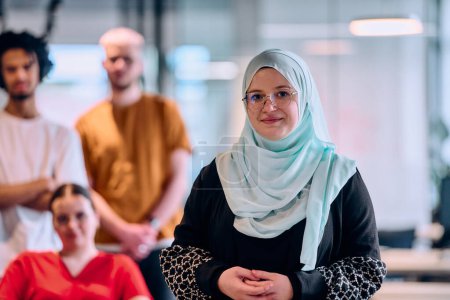 Téléchargez les photos : Un groupe diversifié de jeunes gens d'affaires marchant dans un couloir dans le bureau vitré d'une start-up moderne, y compris une personne en fauteuil roulant et une femme portant un hijab. - en image libre de droit