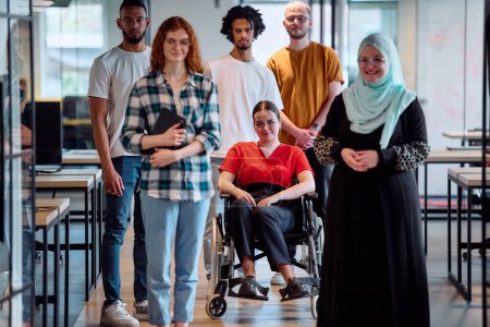 Téléchargez les photos : Un groupe diversifié de jeunes gens d'affaires marchant dans un couloir dans le bureau vitré d'une start-up moderne, y compris une personne en fauteuil roulant et une femme portant un hijab. - en image libre de droit