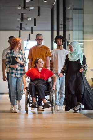 Photo for People walking a corridor in the glass-enclosed office of a modern startup, including a person in a wheelchair and a woman wearing a hijab. - Royalty Free Image