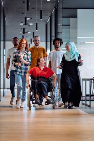 Photo for People walking a corridor in the glass-enclosed office of a modern startup, including a person in a wheelchair and a woman wearing a hijab. - Royalty Free Image