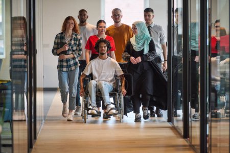 Un grupo diverso de jóvenes empresarios se congrega dentro de una moderna oficina cerrada en cristal de startups, con inclusión con una persona en silla de ruedas, un joven afroamericano y un hiyab.