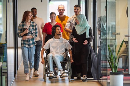 Téléchargez les photos : Un groupe diversifié de jeunes gens d'affaires se rassemble au sein d'un bureau vitré moderne de startups, mettant en vedette l'inclusion avec une personne en fauteuil roulant, un jeune homme afro-américain et un hijab - en image libre de droit