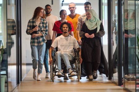 Photo for A diverse group of young business people congregates within a modern startups glass-enclosed office, featuring inclusivity with a person in a wheelchair, an African American young man, and a hijab - Royalty Free Image