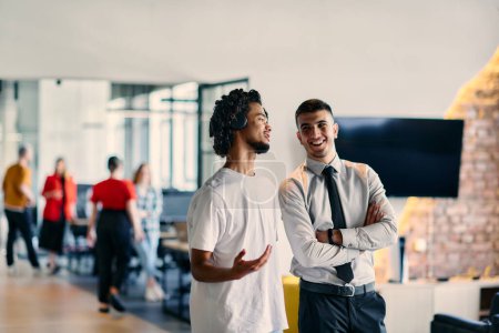 Un grupo de colegas, incluyendo un hombre de negocios afroamericano y un joven líder con camisa y corbata, posan juntos en una moderna oficina del centro de coworking, que representa una mezcla dinámica de