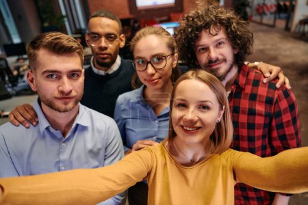 Téléchargez les photos : Un groupe diversifié de professionnels des affaires prennent une pause de leurs tâches dans un bureau de démarrage moderne pour capturer un selfie créatif, mettant en valeur le travail d'équipe et une culture de travail dynamique. - en image libre de droit