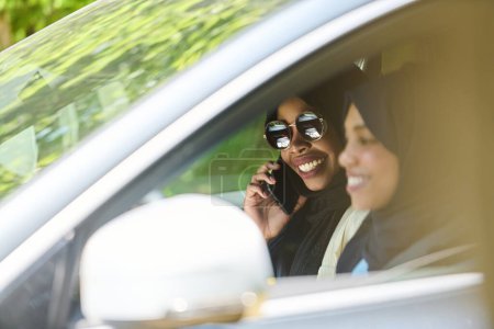Téléchargez les photos : Deux femmes musulmanes portant le hijab conversent sur un smartphone tout en voyageant ensemble dans une voiture à travers le. - en image libre de droit