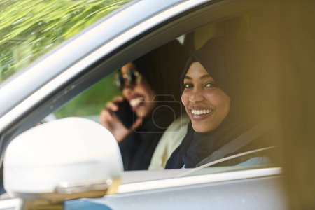 Téléchargez les photos : Deux femmes musulmanes portant le hijab conversent sur un smartphone tout en voyageant ensemble dans une voiture à travers le. - en image libre de droit