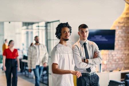 Téléchargez les photos : Un groupe de collègues, dont un homme d'affaires afro-américain et un jeune leader en chemise et cravate, posent ensemble dans un bureau moderne de centre de coworking, représentant un mélange dynamique de - en image libre de droit