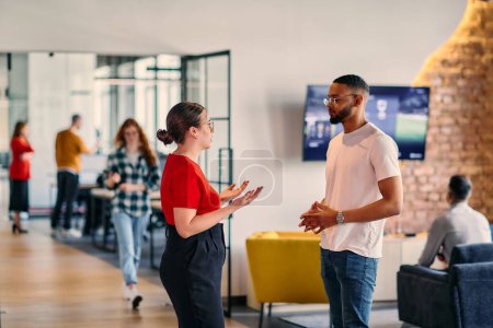 Young business colleagues, including an African American businessman, engage in a conversation about business issues in the hallway of a modern startup coworking center